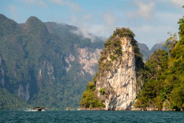 Khao Sok Ulusal Parkı, Tayland 'daki yeşil ormanlarla kaplı kireçtaşı uçurumları. Mavi göl ve uzun kuyruk teknesi, mavi gökyüzü. Yüksek kalite fotoğraf