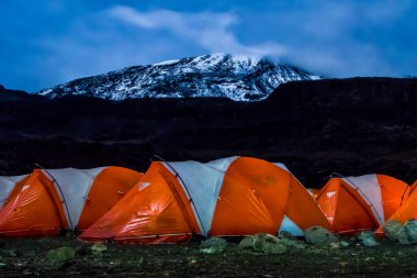 Kilimanjaro Dağı 'ndan önce gece boyunca turuncu çadırlar içeriden aydınlatıldı. Yıldızlar ve Samanyolu görünür. Yüksek kalite fotoğraf