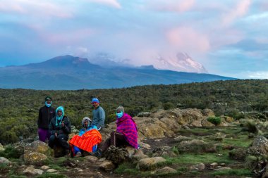 Kilimanjaro Dağı bulutların arasında yerli hamallarla mola verirken görülüyor. Üstü karla kaplı, gün batımında dramatik bir ruh hali. Yüksek kalite fotoğraf