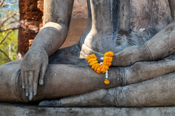Detail of Buddha statue covered with orange offering flowers in Sukhothai Historical Park, Thailand. Grand Buddha statues. No people. High quality photo