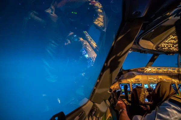 Pilot view of a Boeing 737 cockpit during cruise flight at night. Detailed instruments, autopilot, yoke. Shoulder of pilot with insignia. Reflection of cockpit in the side window. High quality photo