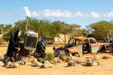 Paslı, terk edilmiş araba enkazları çölde, Solitaire 'de, Namibya' da, Afrika 'da. Parlak mavi gökyüzünün altındaki kırmızı pas ile renkli traktör enkazı. Toprak yol, kayalar, akasya ağacı ve kırmızı kumullar. Yüksek kalite fotoğraf