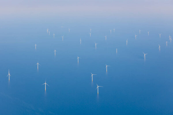 Aerial view of offshore wind farm with wind turbines on the North Sea, the Netherlands, Europe. Several large white and yellow wind turbines, wind mills on a blue, calm, flat sea. High quality photo
