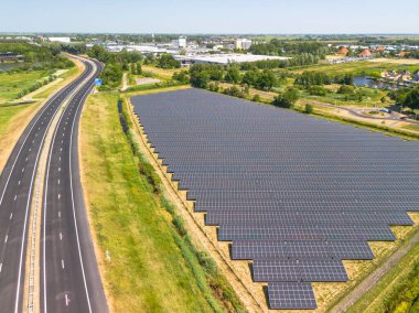 Sneek, Friesland 'a giden yolun yakınındaki güneş enerjisi çiftliğindeki gras üzerindeki güneş panellerinin hava görüntüsü. Büyük mavi fotovoltaik hücreler alanı, PV sistemi veya güneş panelleri. 4 şeritli yol. Yüksek kalite fotoğraf