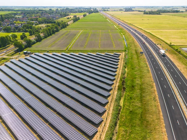 stock image Aerial view of solar panels on gras in solar energy farm near road to Sneek, Friesland. Large field of blue photovoltaic cells, the PV system or solar panels. 4 lane highway. High quality photo