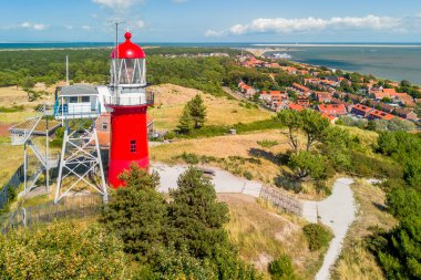 Vlieland 'in hava aracı görüntüsü. Küçük bir kasabanın, Kuzey Denizi 'nin ve Wadden Denizi' nin üzerindeki kumulun tepesindeki parlak kırmızı deniz feneriyle aydınlık bir yaz günü. Yüksek kalite fotoğraf