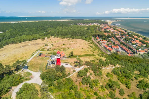 Vlieland 'in hava aracı görüntüsü. Küçük bir kasabanın, Kuzey Denizi 'nin ve Wadden Denizi' nin üzerindeki kumulun tepesindeki parlak kırmızı deniz feneriyle aydınlık bir yaz günü. Yüksek kalite fotoğraf