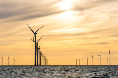 Yüksek yel değirmenleri, IJsselmeer, Hollanda 'nın kıyı rüzgâr tarlaları. Huysuz bulutlu turuncu akşam gökyüzü.
