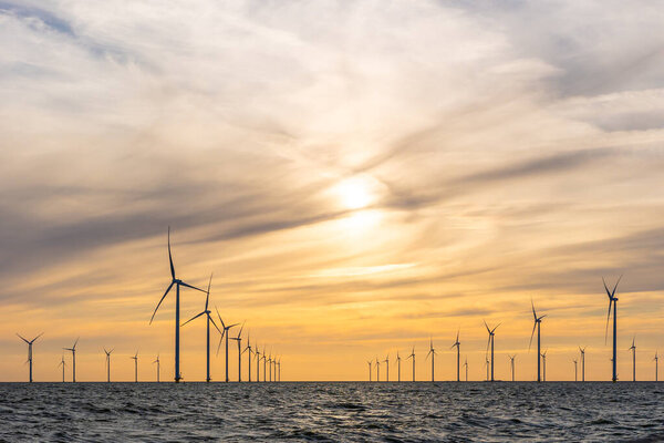 Оффшорная ветряная электростанция с множеством изогнутых рядов высоких ветряных мельниц, Эйсселмер, Нидерланды. Оранжевое вечернее небо с мрачными облаками.