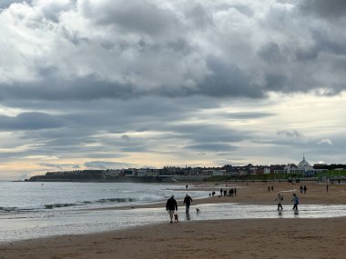 İngiltere, Newcastle 'daki Whitley Körfezi' nde kumlu ve dalgalı sahilde kara dramatik yağmur bulutları. Tipik yağmurlu İngiliz havası. İnsanlar sahilde köpeği gezdiriyorlar.. 