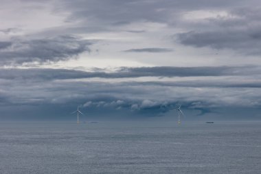 İki büyük yel değirmeni, alternatif yeşil, yenilenebilir enerji için türbinler, elektrik, sadece İngiliz kıyılarında uçurumlar ve dramatik bulutlar. Whitley Bay, Newcastle, İngiltere. Yüksek kalite fotoğraf
