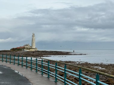 St. Marys Lighthouse with basalt path at low tide with a large offshore windmill at sea, just of the English coast. Light blue retro, antique, art deco cast iron handrail. Whitley Bay, Newcastle, UK. clipart