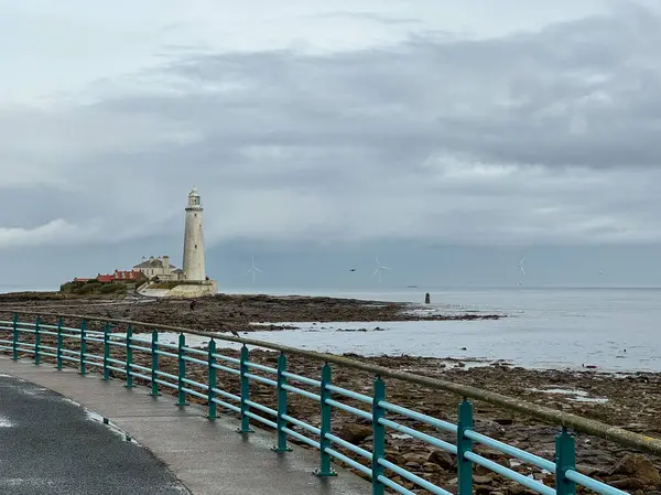St. Marys Deniz Feneri. Akıntıya kapılmış bazalt yolu var. Denizde büyük bir yel değirmeni var. Açık mavi retro, antika, sanat deco döküm demir tırabzan. Whitley Körfezi, Newcastle, İngiltere.