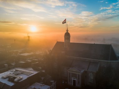 Gündoğumunda kilisenin tepesinde Hollanda bayrağıyla Sneek kasabasında insansız hava aracı görüntüsü. Parlak turuncu renkler ve şehrin sokaklarında biraz sis. Yüksek kalite fotoğraf