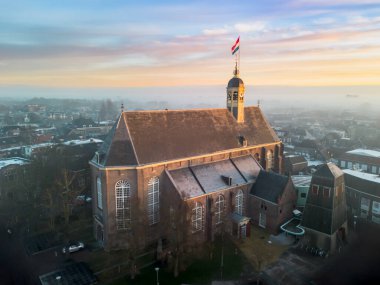Gündoğumunda kilisenin tepesinde Hollanda bayrağıyla Sneek kasabasında insansız hava aracı görüntüsü. Parlak turuncu renkler ve şehrin sokaklarında biraz sis. Yüksek kalite fotoğraf