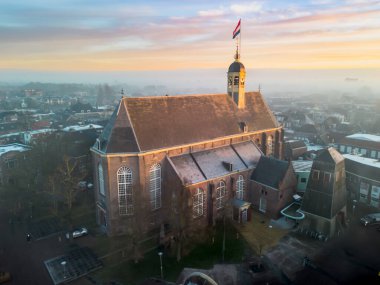 Gündoğumunda kilisenin tepesinde Hollanda bayrağıyla Sneek kasabasında insansız hava aracı görüntüsü. Parlak turuncu renkler ve şehrin sokaklarında biraz sis. Yüksek kalite fotoğraf