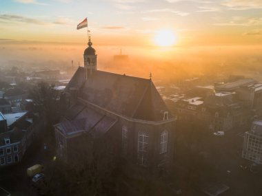 Gündoğumunda kilisenin tepesinde Hollanda bayrağıyla Sneek kasabasında insansız hava aracı görüntüsü. Parlak turuncu renkler ve şehrin sokaklarında biraz sis. Yüksek kalite fotoğraf