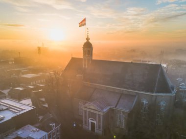 Gündoğumunda kilisenin tepesinde Hollanda bayrağıyla Sneek kasabasında insansız hava aracı görüntüsü. Parlak turuncu renkler ve şehrin sokaklarında biraz sis. Yüksek kalite fotoğraf