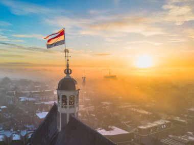 Gündoğumunda kilisenin tepesinde Hollanda bayrağıyla Sneek kasabasında insansız hava aracı görüntüsü. Parlak turuncu renkler ve şehrin sokaklarında biraz sis. Yüksek kalite fotoğraf