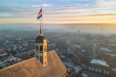 Gündoğumunda kilisenin tepesinde Hollanda bayrağıyla Sneek kasabasında insansız hava aracı görüntüsü. Parlak turuncu renkler ve şehrin sokaklarında biraz sis. Yüksek kalite fotoğraf