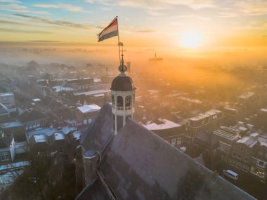 Gündoğumunda kilisenin tepesinde Hollanda bayrağıyla Sneek kasabasında insansız hava aracı görüntüsü. Parlak turuncu renkler ve şehrin sokaklarında biraz sis. Yüksek kalite fotoğraf