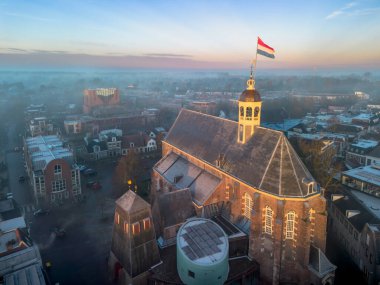 Gündoğumunda kilisenin tepesinde Hollanda bayrağıyla Sneek kasabasında insansız hava aracı görüntüsü. Parlak turuncu renkler ve şehrin sokaklarında biraz sis. Yüksek kalite fotoğraf