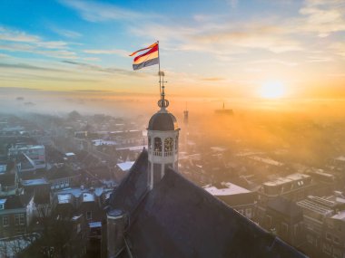 Gündoğumunda kilisenin tepesinde Hollanda bayrağıyla Sneek kasabasında insansız hava aracı görüntüsü. Parlak turuncu renkler ve şehrin sokaklarında biraz sis. Yüksek kalite fotoğraf