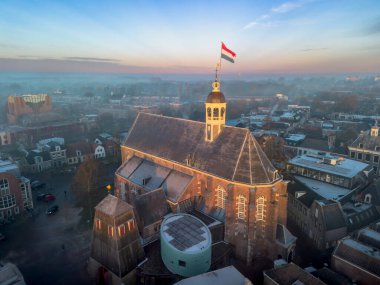 Gündoğumunda kilisenin tepesinde Hollanda bayrağıyla Sneek kasabasında insansız hava aracı görüntüsü. Parlak turuncu renkler ve şehrin sokaklarında biraz sis. Yüksek kalite fotoğraf