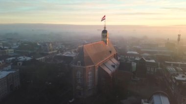 Gündoğumunda kilisenin tepesinde Hollanda bayrağıyla Sneek kasabasında insansız hava aracı görüntüsü. Parlak turuncu renkler ve şehrin sokaklarında biraz sis. Yüksek kalite 4K görüntü