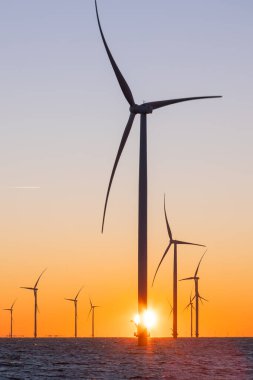 Off shore wind turbines or wind mills at sea during sunrise. Many high windturbines with a orange rising sun. High quality photo clipart