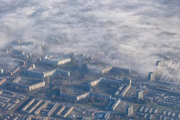 空中高空城市的图像 地面上覆盖着一层雾气或雾气 清晨柔和的阳光 云彩覆盖了城镇的房屋和公寓 高质量的照片 免版税图库照片