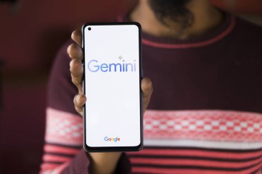 Dhaka, Bangladesh - 27 December 2023: Hand holding a phone with Google Gemini AI chatbot Gemini is a family of multimodal large language models developed by Google. clipart