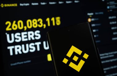 Dhaka, Bangladeş - 02 Mart 2025: Binance logosu bir akıllı telefon ekranında gösteriliyor ve arkaplanda bir bilgisayar ekranında binance web sitesi görülüyor.