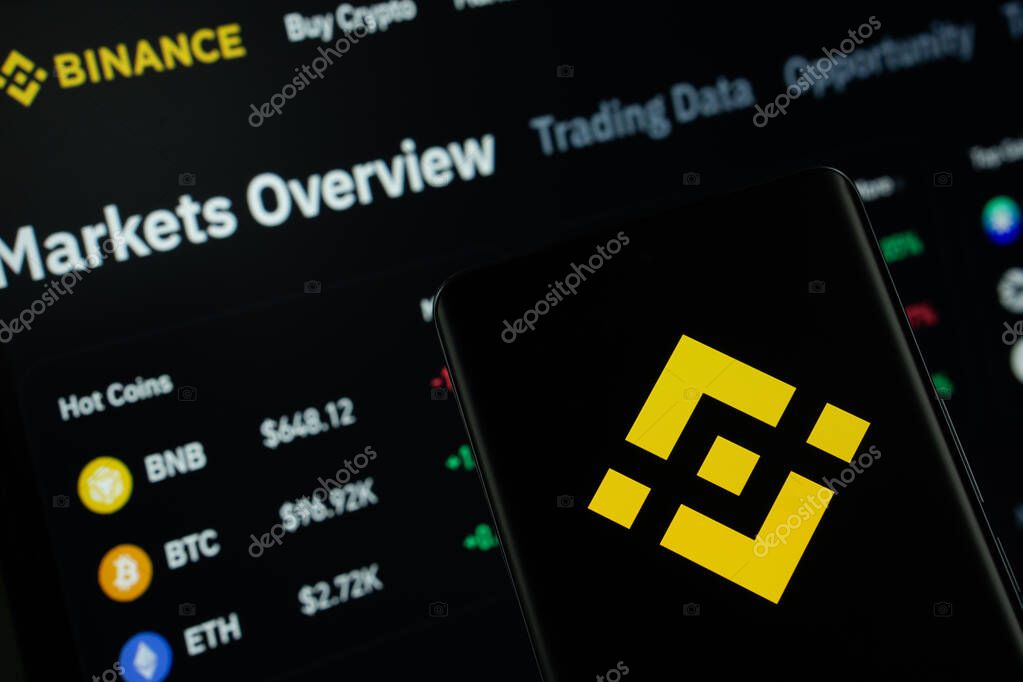 Dhaka, Bangladesh- 02 March 2025: Binance logo is displayed on a smartphone screen, with the binance website visible on a computer screen in the background.