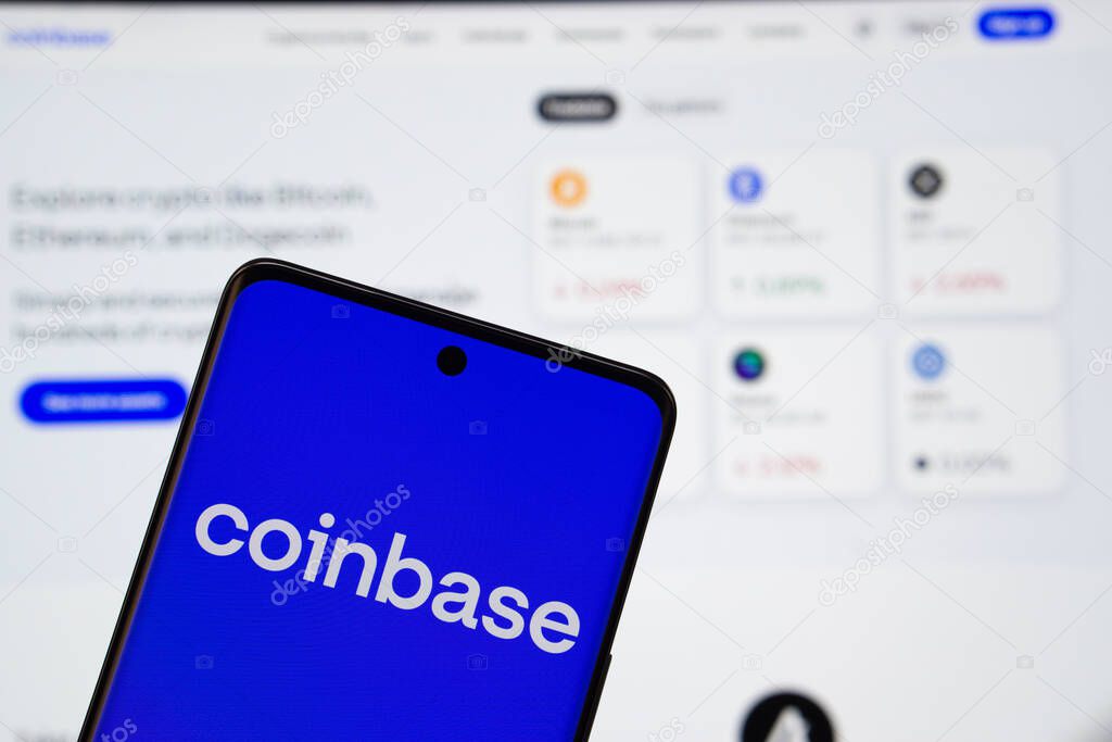 Dhaka, Bangladesh- 05 March 2025: Coinbase logo is displayed on a smartphone screen, with the coinbase website visible on a computer screen in the background.