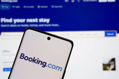 Dhaka, Bangladeş - 05 Mart 2025: Booking.com logosu bir akıllı telefon ekranında sergilenirken, Booking.com web sitesi arka planda bir bilgisayar ekranında görünür.
