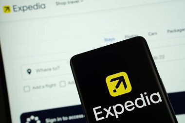 Dhaka, Bangladeş - 08 Mart 2025: Expedia logosu bir akıllı telefon ekranında gösteriliyor, arka planda bilgisayar ekranında ekspedisyon web sitesi görülüyor.