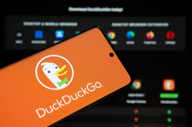 Dhaka, Bangladeş - 08 Mart 2025: DuckGo logosu bir akıllı telefon ekranında gösteriliyor, DuckDuckGo web sitesi arka planda bir bilgisayar ekranında görünüyor.