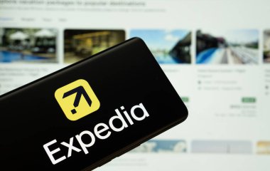 Dhaka, Bangladeş - 08 Mart 2025: Expedia logosu bir akıllı telefon ekranında gösteriliyor, arka planda bilgisayar ekranında ekspedisyon web sitesi görülüyor.