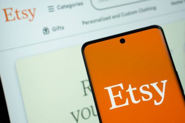 Dhaka, Bangladeş - 08 Mart 2025: Etsy logosu bir akıllı telefon ekranında gösteriliyor ve Etsy web sitesi arka planda bir bilgisayar ekranında görülüyor.
