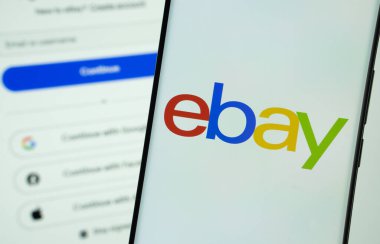 Dhaka, Bangladeş - 16 Mart 2025: ebay logosu bir akıllı telefon ekranında gösterilir, ebay giriş sayfası arka planda bir bilgisayar ekranında görünür..