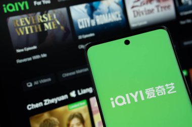 Dhaka, Bangladeş - 17 Mart 2025: Iqiyi logosu akıllı telefon ekranında gösteriliyor ve Iqiyi web sitesi arka planda bir bilgisayar ekranında görülebiliyor.