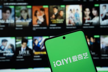 Dhaka, Bangladeş - 17 Mart 2025: Iqiyi logosu akıllı telefon ekranında gösteriliyor ve Iqiyi web sitesi arka planda bir bilgisayar ekranında görülebiliyor.