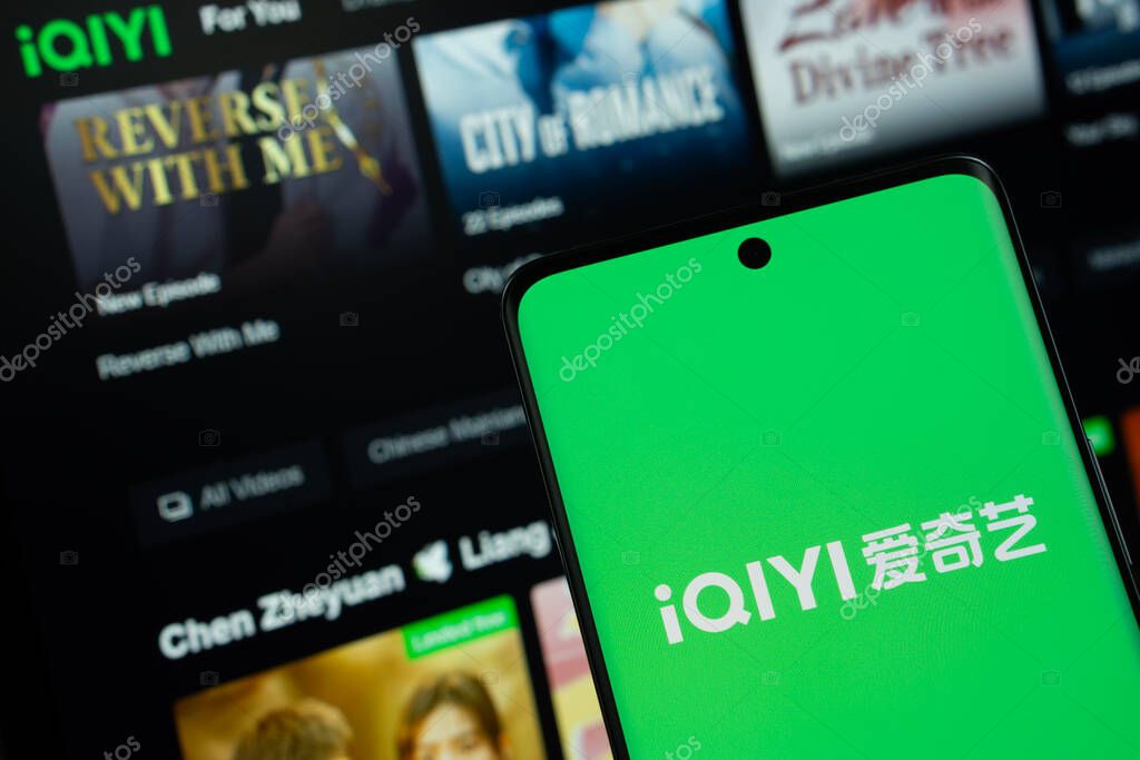 Dhaka, Bangladesh - 17 March 2025: The logo of the iqiyi is displayed on a smartphone screen, and the website iqiyi is visible on a computer screen in the background.