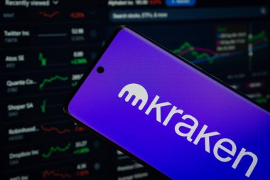 Dhaka, Bangladeş - 17 Mart 2025: Kraken logosu bir akıllı telefon ekranında sergilenmektedir, arka planda bir bilgisayar ekranında bir stok grafik web sayfası görünür.