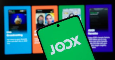 Dhaka, Bangladeş - 17 Mart 2025: Joox logosu akıllı telefon ekranında gösteriliyor ve web sitesi joox arka plandaki bilgisayar ekranında görülebiliyor.