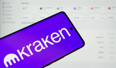 Dhaka, Bangladeş - 17 Mart 2025: Kraken logosu bir akıllı telefon ekranında sergilenmektedir, arka planda bir bilgisayar ekranında bir stok grafik web sayfası görünür.