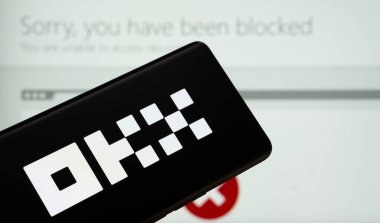 Dhaka, Bangladeş - 17 Mart 2025: Okx logosu akıllı telefon ekranında gösteriliyor ve okx web sitesi arka planda bir bilgisayar ekranında görülebiliyor.