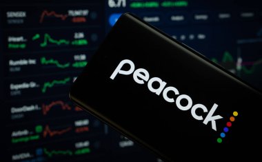 Dhaka, Bangladeş - 17 Mart 2025: Tavus kuşu logosu bir akıllı telefon ekranında sergilenmektedir, arka planda bir bilgisayar ekranında bir stok grafik web sayfası görünür..