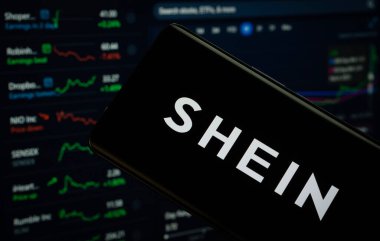 Dhaka, Bangladeş - 18 Mart 2025: Shein logosu bir akıllı telefon ekranında gösteriliyor, arka planda bilgisayar ekranında bir stok grafik web sayfası görülüyor.